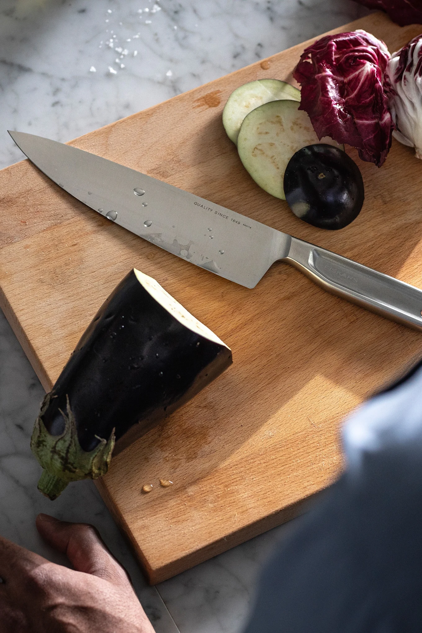 Das All Steel-Küchenmesser von Fiskars liegt neben einer Aubergine auf einem Schneidebrett.