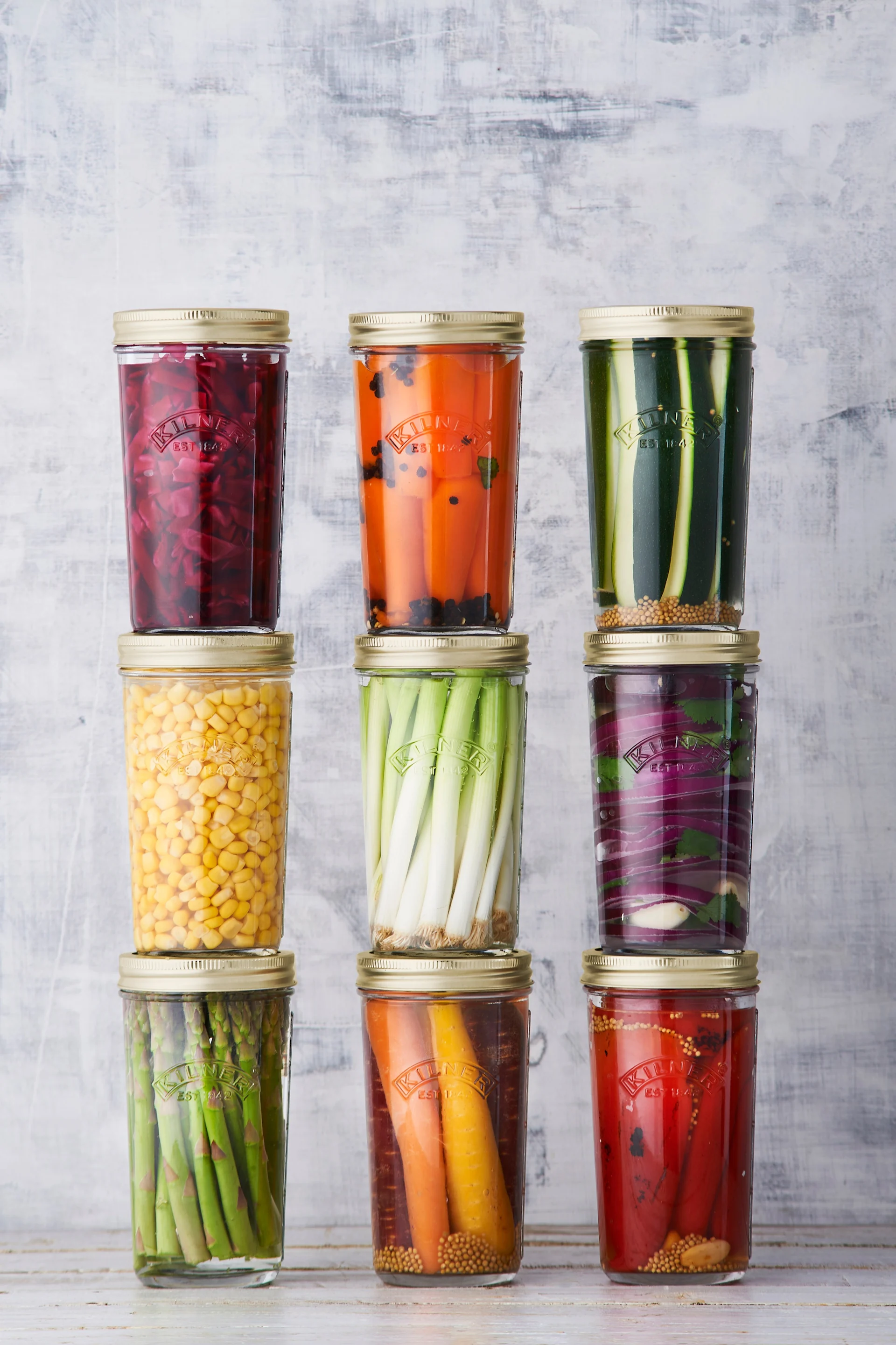 Neun Gläser mit eingelegtem Gemüse: Rote Bete, Karotten, Zucchini, Mais, Frühlingszwiebeln, Rotkohl, Spargel und Paprika.