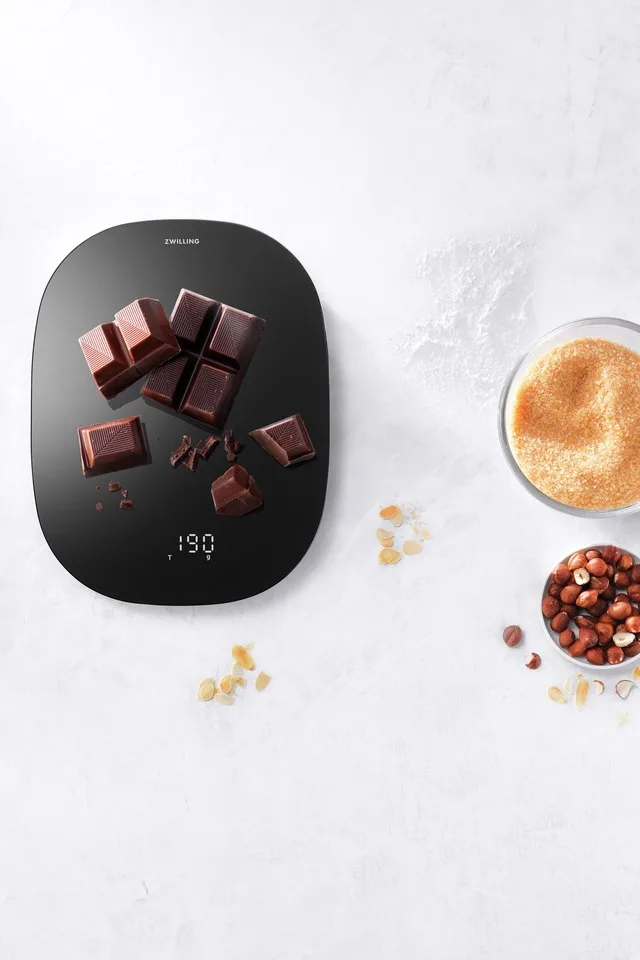 Auf der schwarzen digitalen Küchenwaage von Zwilling wird Schokolade abgewogen.