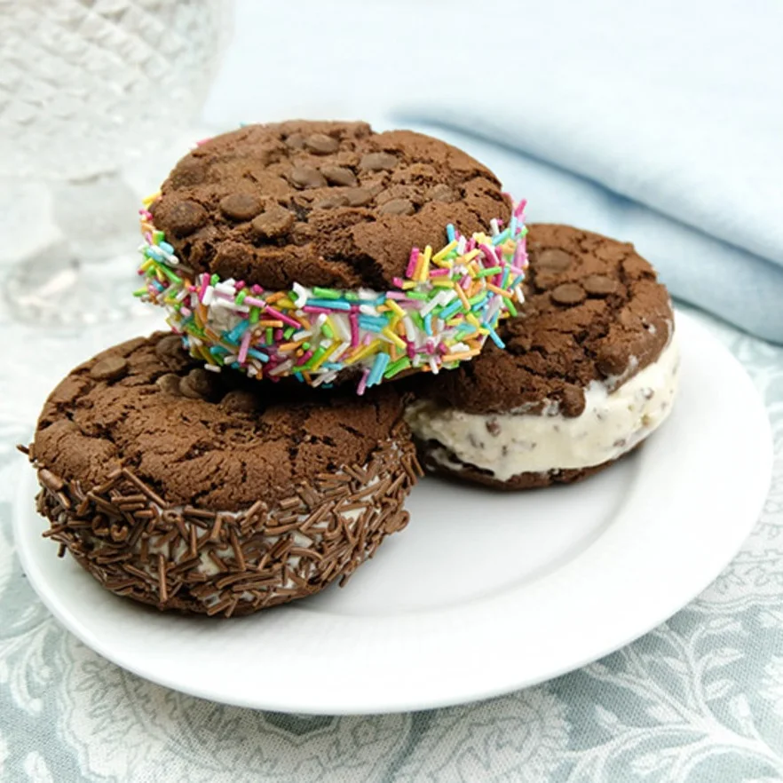Drei Schokoladenkeks-Eis-Sandwiches. Eines mit bunten Streuseln, eines mit Schokoladenstreuseln.
