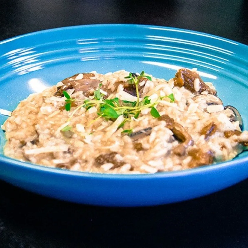 Pilzrisotto mit geriebenem Käse und frischen Kräutern in einer blauen Schüssel.