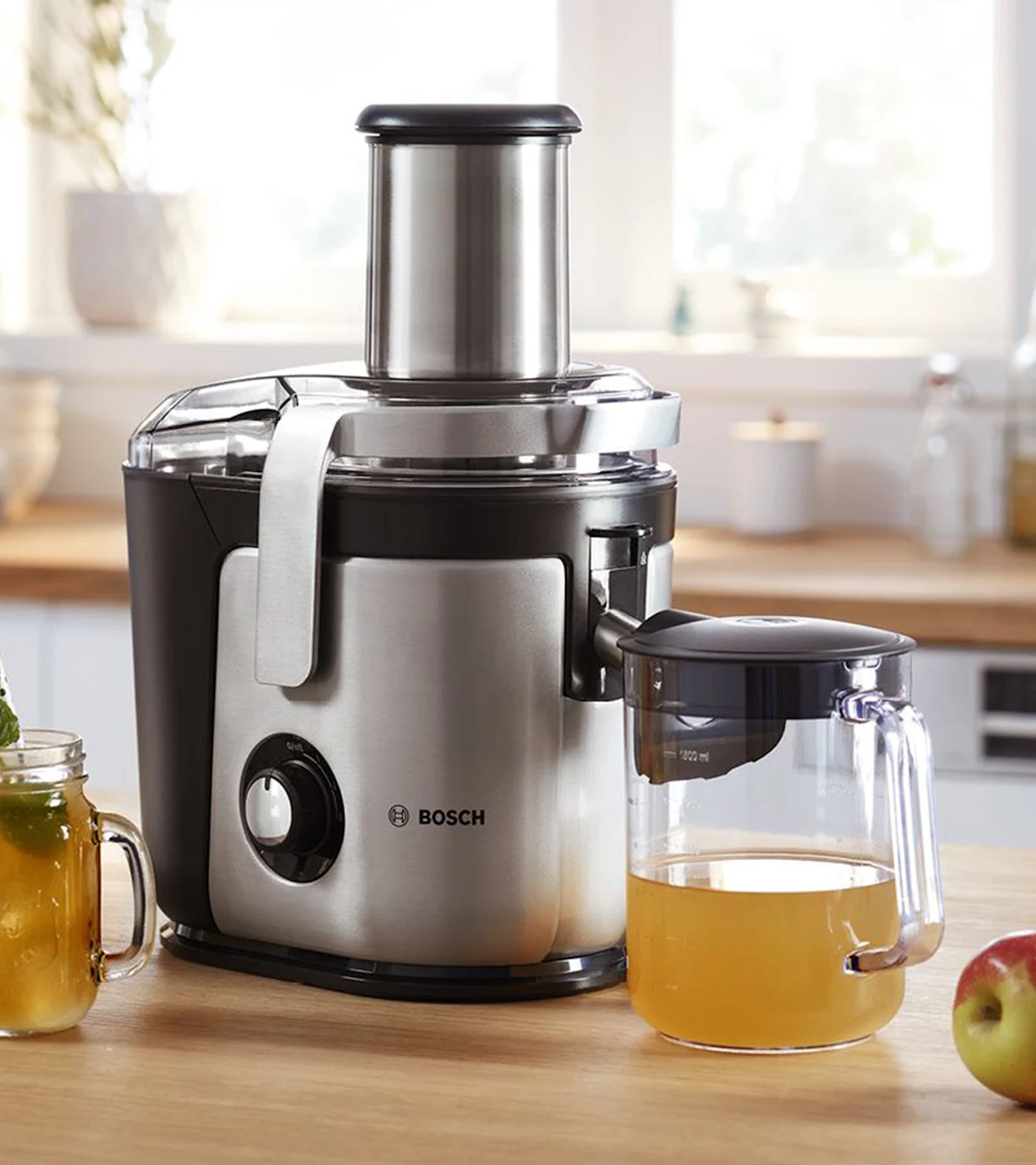 Bosch Entsafter, silber und schwarz, auf einer Küchentheke mit einem Krug Apfelsaft und einem Apfel.