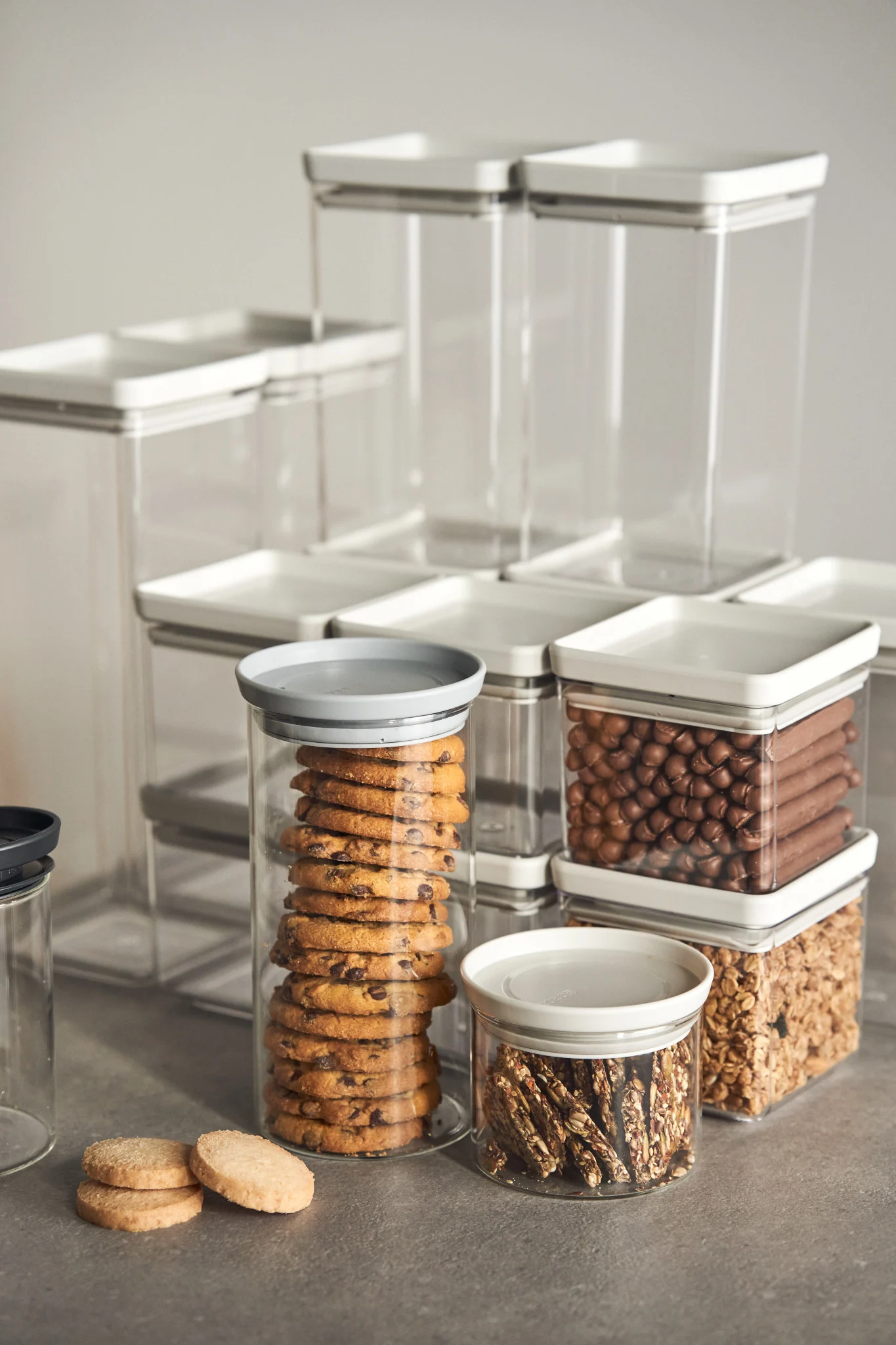 Verschiedene durchsichtige Lebensmittelbehälter, einige gefüllt mit Keksen, Schokoriegeln, Schokosnacks und Müsli.