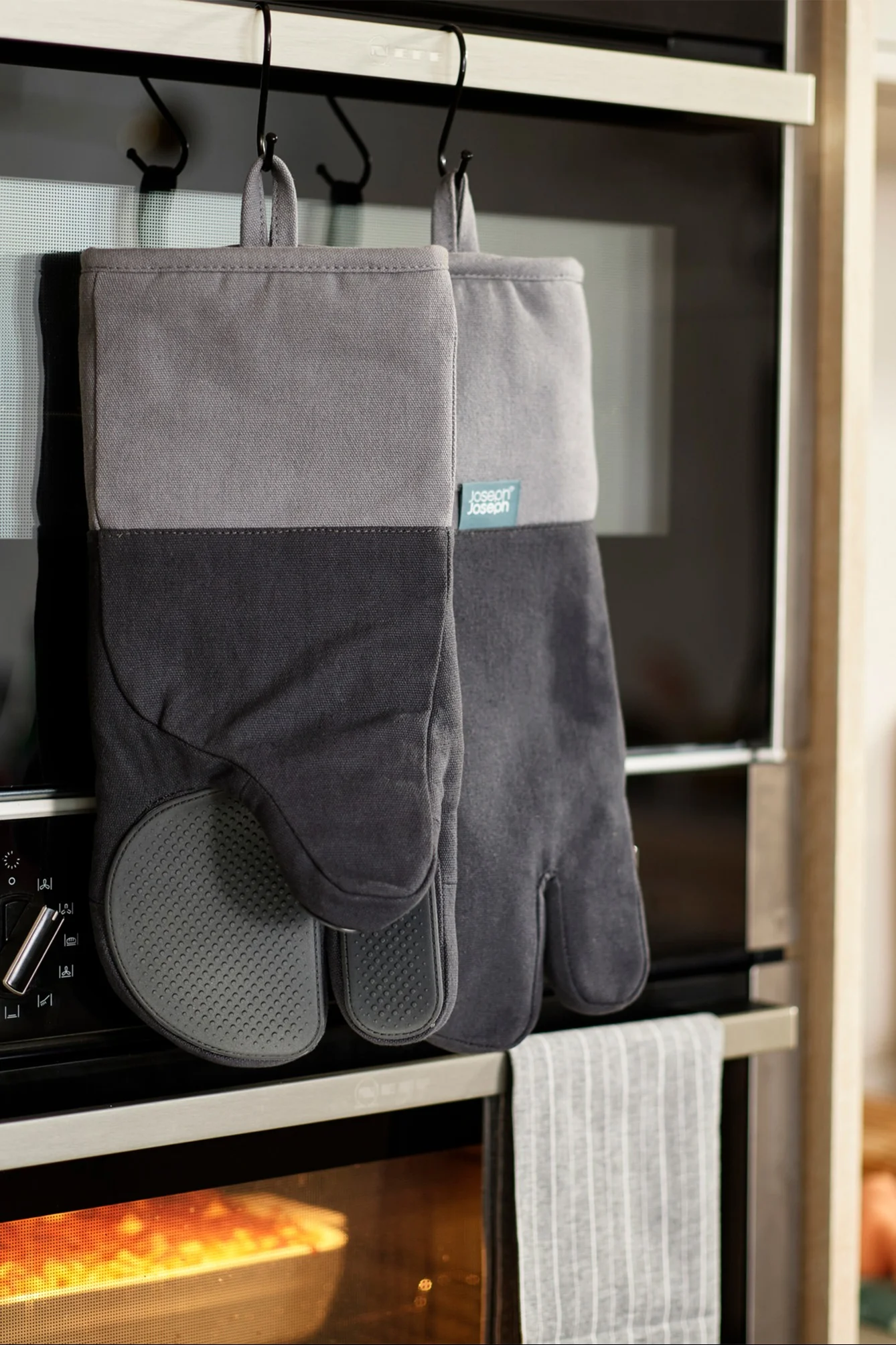 Graue und schwarze Ofenhandschuhe hängen an Haken über einem Ofen, in dem Speisen backen.