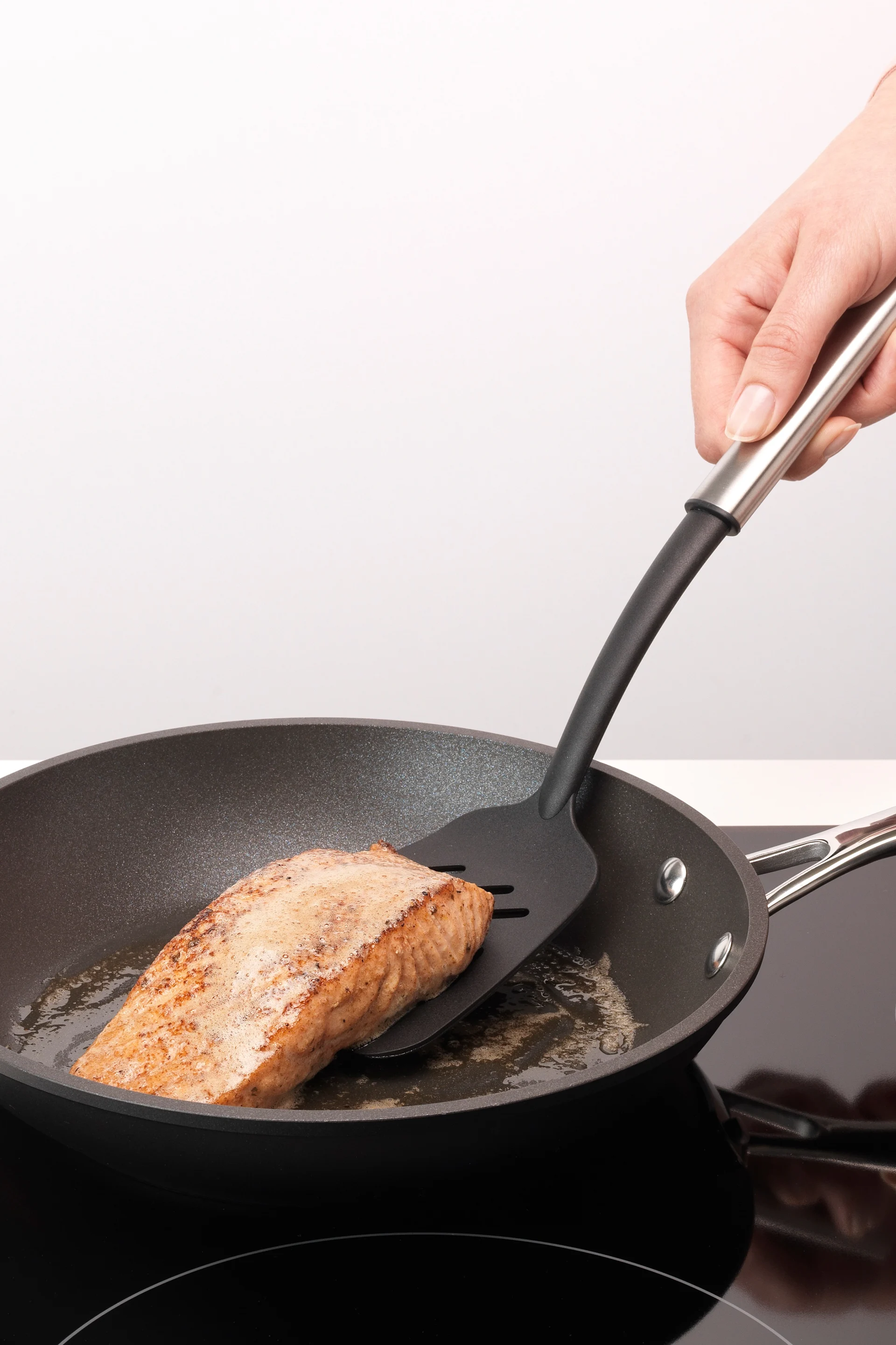Lachs wird in einer Pfanne gebraten und mit einem Pfannenwender gewendet.