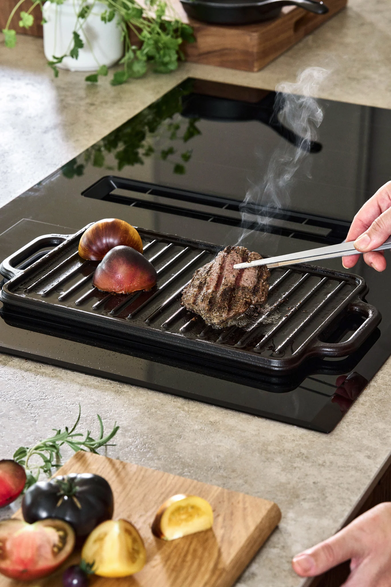 Eine gusseiserne Bratpfanne auf einem Induktionskochfeld mit ein paar Tomaten und einem Steak. 