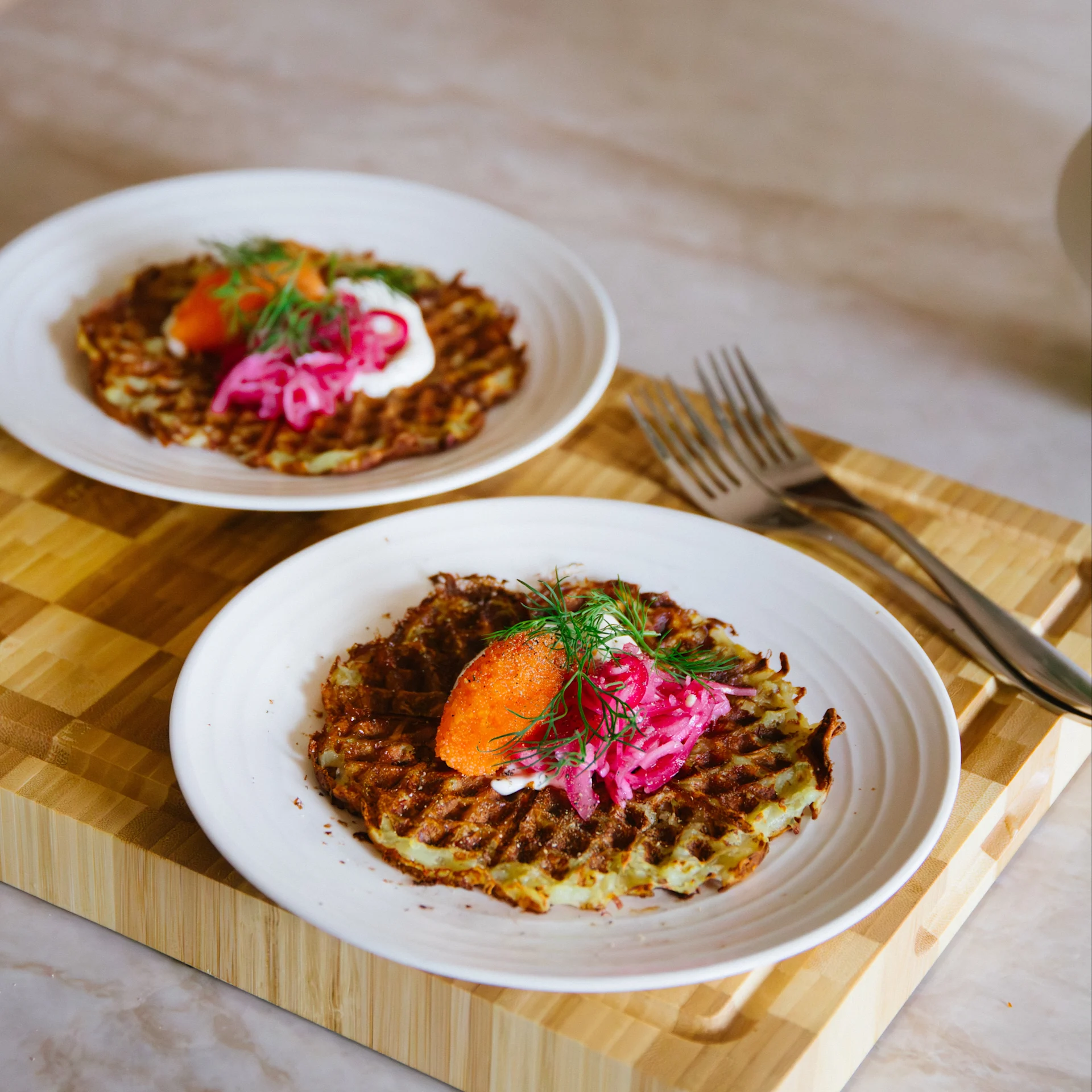 Zwei Teller herzhafte Waffeln mit orangefarbenem Rogen, weißer Creme, eingelegten roten Zwiebeln und Dill.