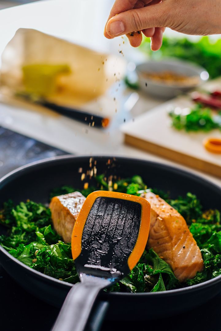 Der Pfannenwender Functional Form von Fiskars liegt auf einer Pfanne mit Fisch und Spinat darin.