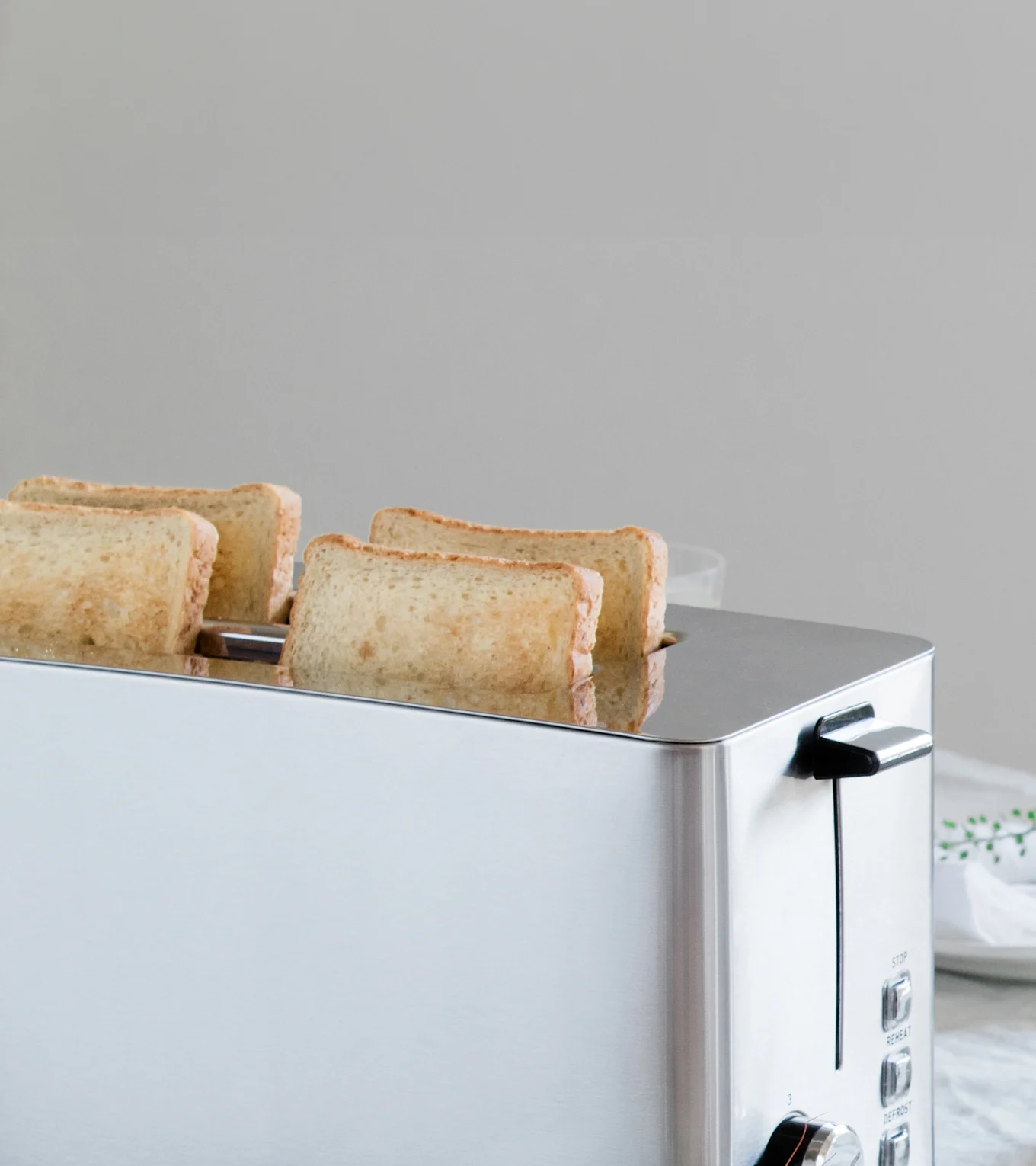 Ein silberner Toaster mit vier leicht gerösteten Brotscheiben, die teilweise aus seinen Schlitzen ragen.