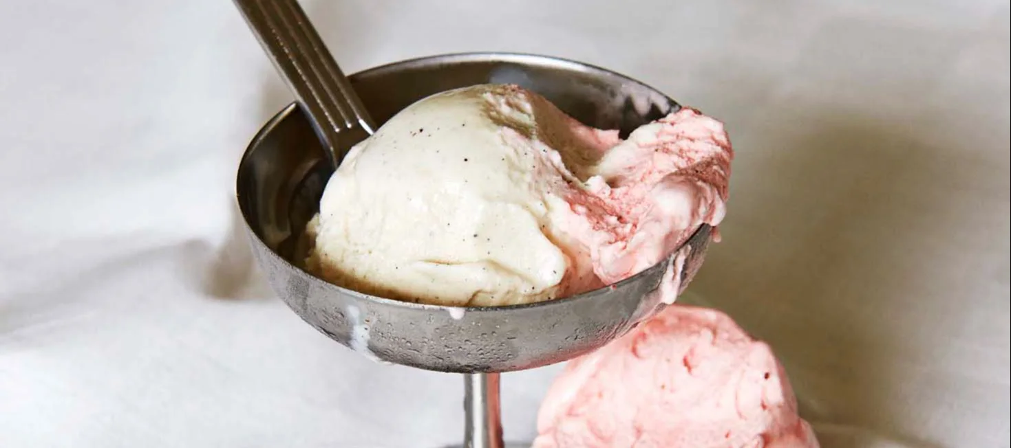 Zwei Kugeln Eis, Vanille und Erdbeere, in einem Metall-Eisbecher mit Löffel.