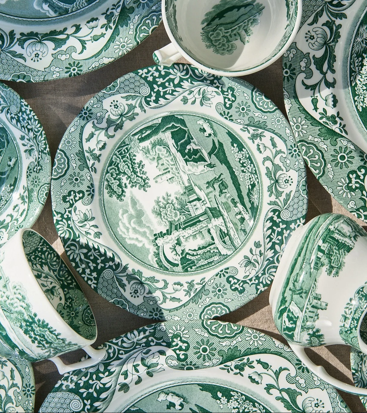 Ansicht von oben auf verschiedene grün-weiß gemusterte Keramikteller und Tassen mit aufwendigen Landschafts- und Blumenmotiven.