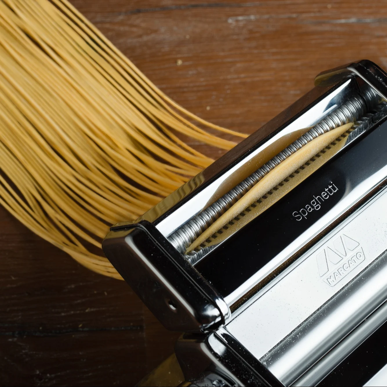 Nudelmaschine extrudiert frische Spaghettistränge auf einer Holzoberfläche.