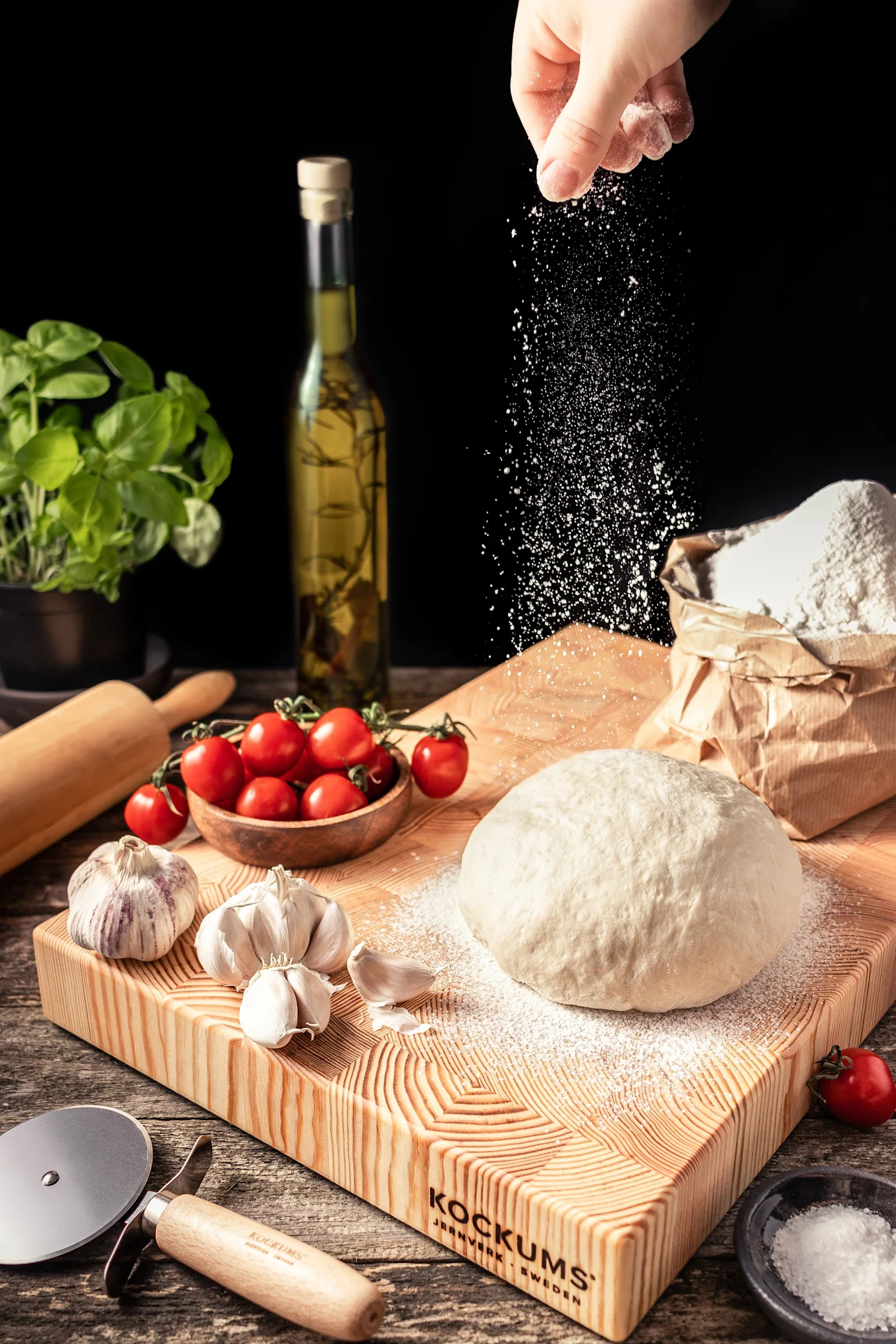 Auf dem Schneidebrett von Kockum liegt Pizzateig, daneben Tomaten und Knoblauch.