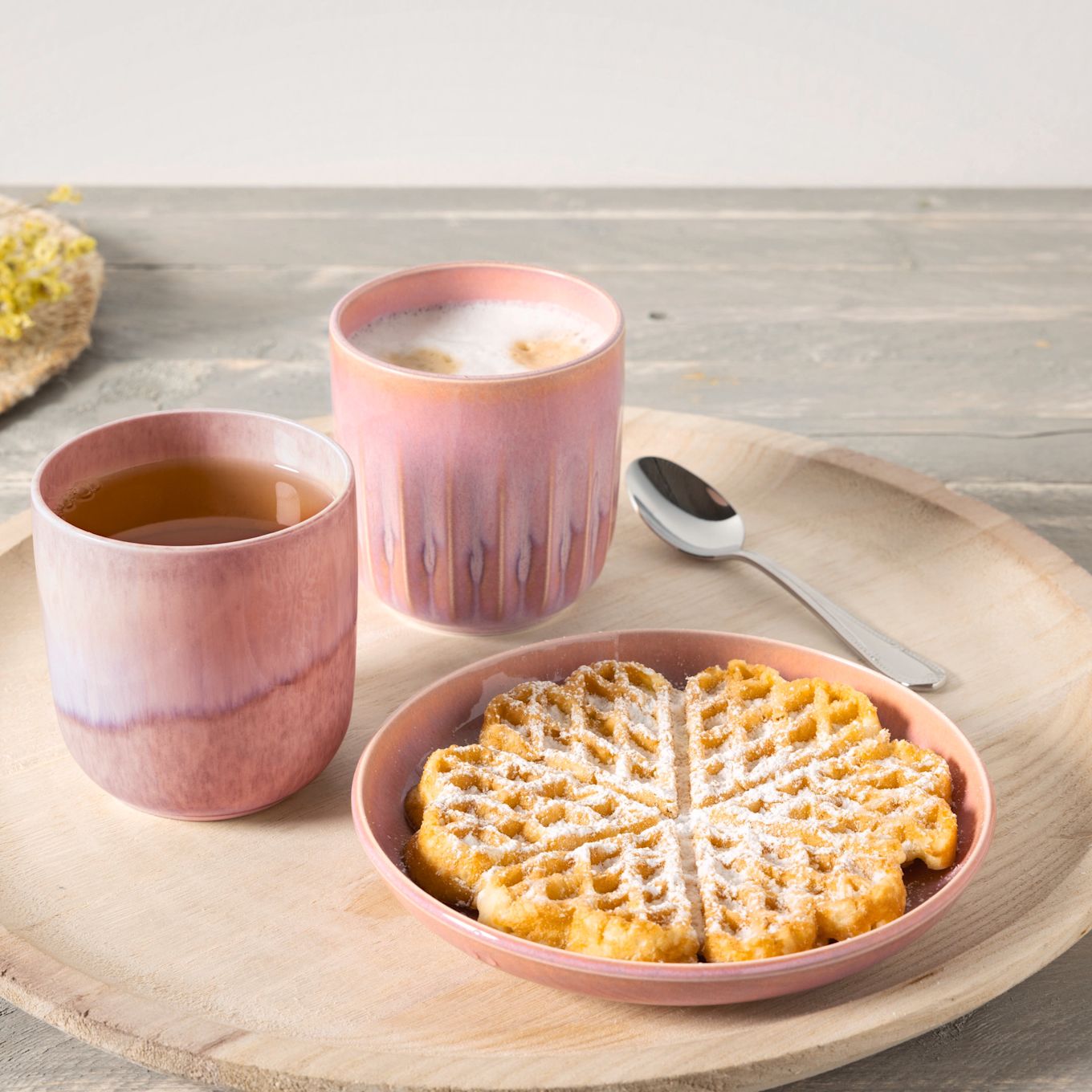Waffeln sind vielseitig und können süß oder salzig serviert werden. Hier sehen Sie eine Waffel mit Puderzucker bestäubt, daneben ein Becher mit Kaffee und einer mit Tee aus der Perlemor-Kollektion von Villeroy & Boch.