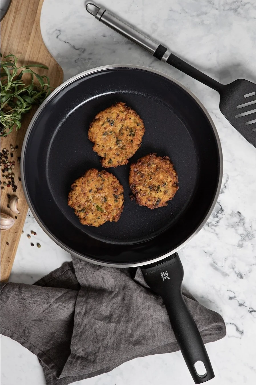Hier sehen Sie die PermaDur Premium Bratpfanne von WMF mit Bratlingen auf einer Küchenanrichte.