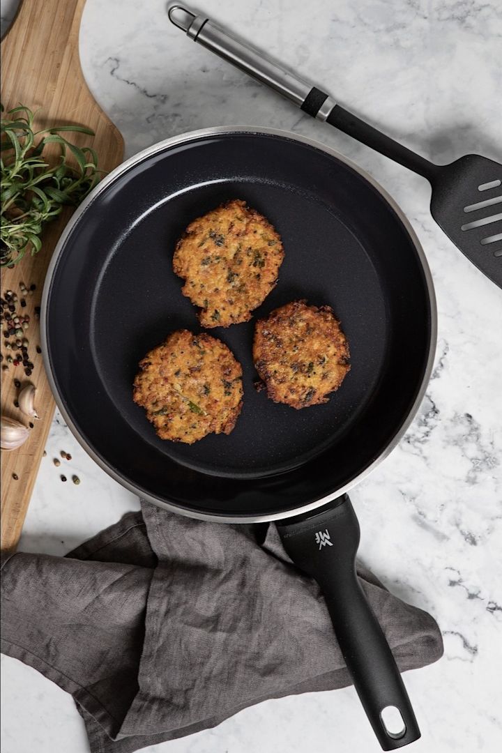 Hier sehen Sie die PermaDur Premium Bratpfanne von WMF mit Bratlingen auf einer Küchenanrichte.