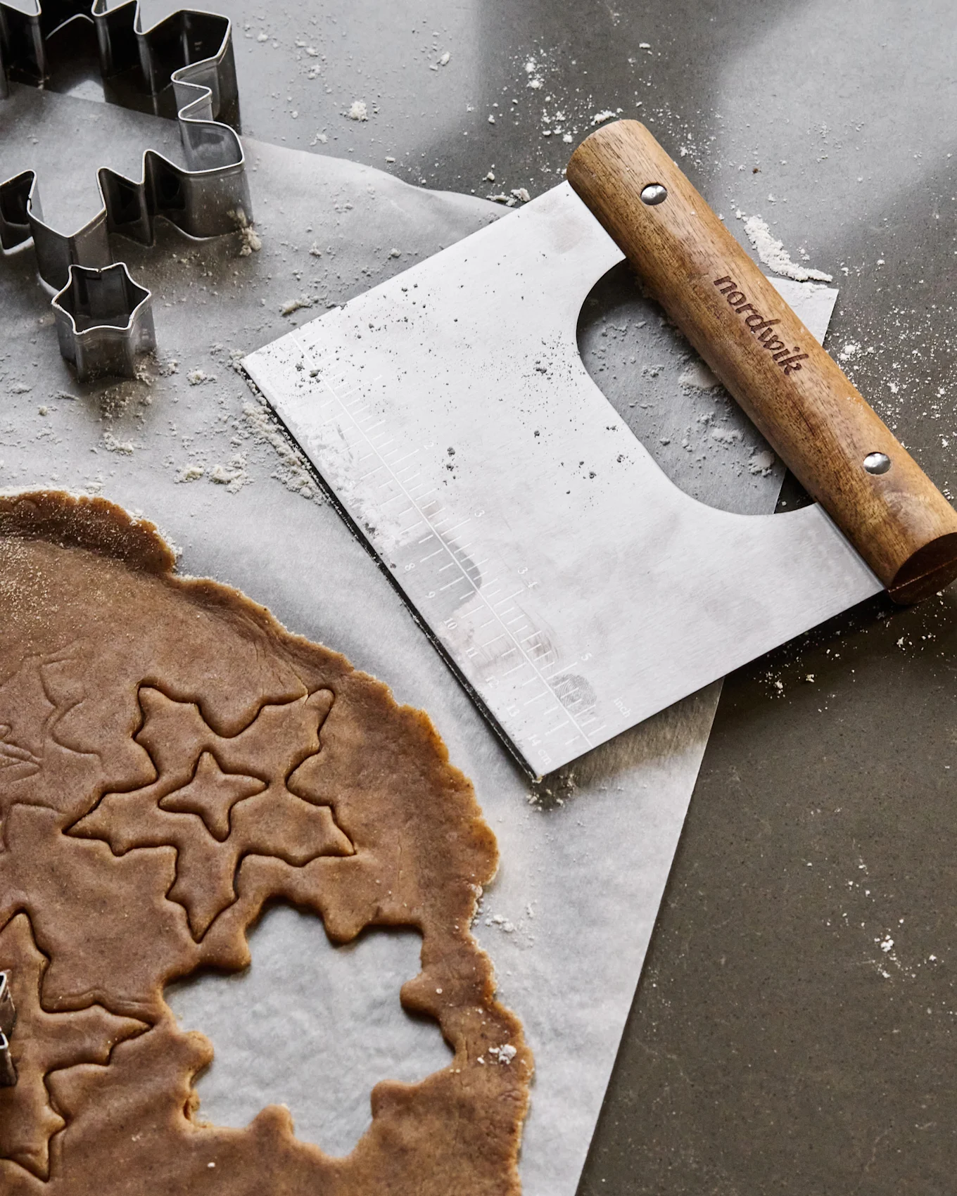 Lebkuchenteig mit Stern- und Blattformen, Metall-Ausstechformen und einem Teigschaber auf einer bemehlten Oberfläche.