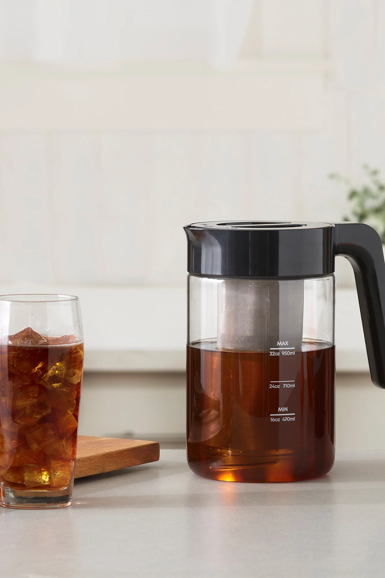 Eine Glaskaraffe mit schwarzem Deckel und Sieb enthält Cold Brew Kaffee neben einem Glas Eiskaffee.