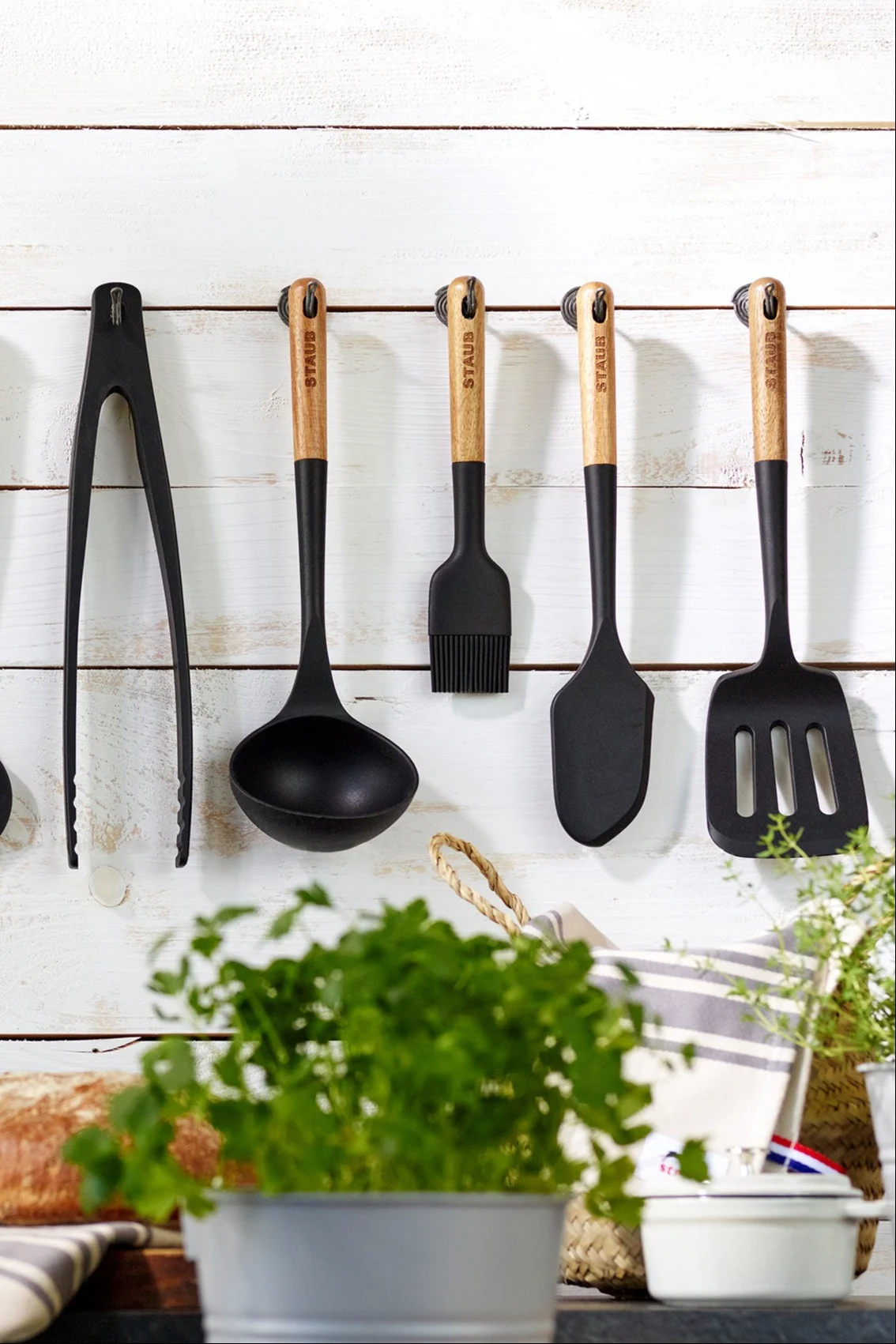 Bratspachtel, Kelle, Zange und weitere nützliche Küchenutensilien hängen nebeneinander an einer Wand in einer Küche.