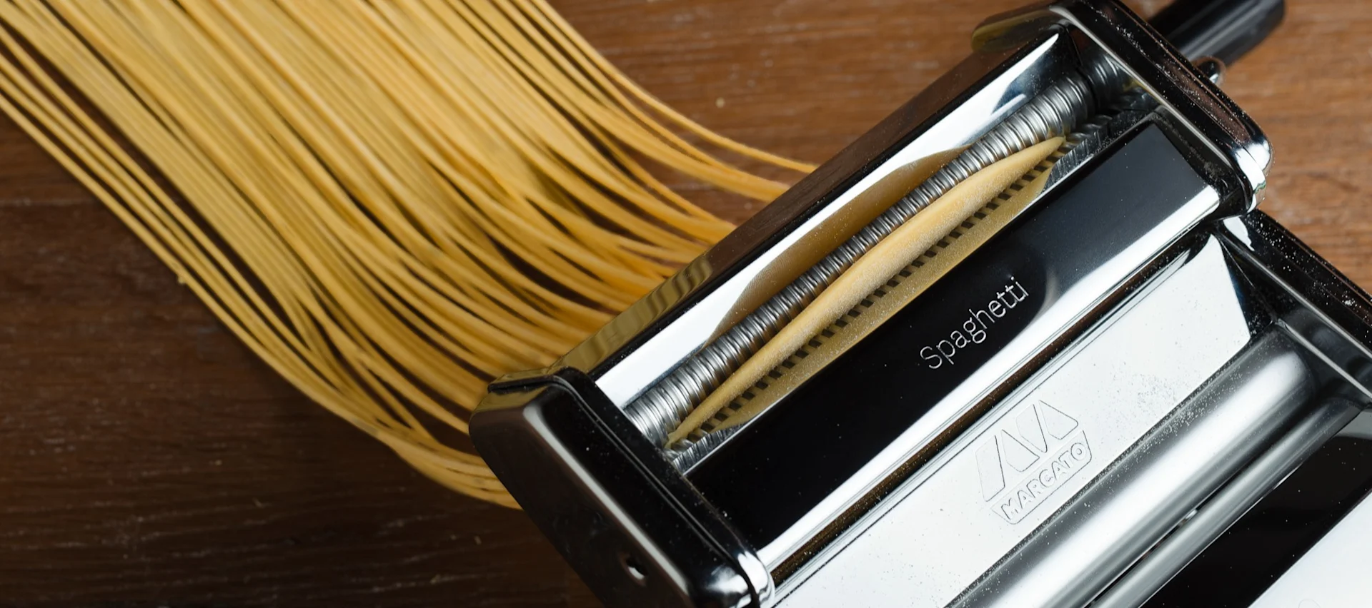 Frisch zubereitete Spaghetti kommen aus einer Nudelmaschine auf eine Holzfläche.