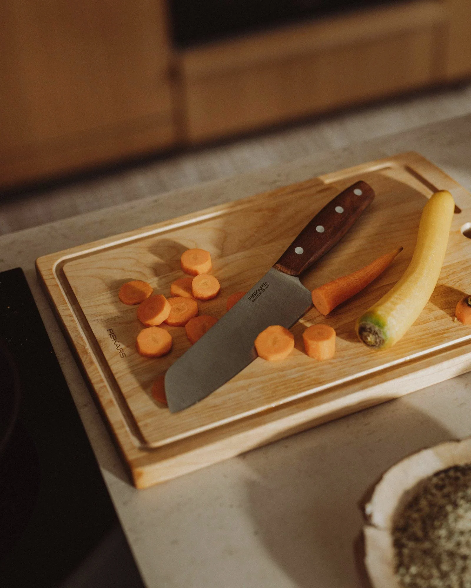 Ein Holzschneidebrett mit geschnittenen orangen Karotten, einer ganzen gelben Karotte und einem Messer mit Holzgriff.