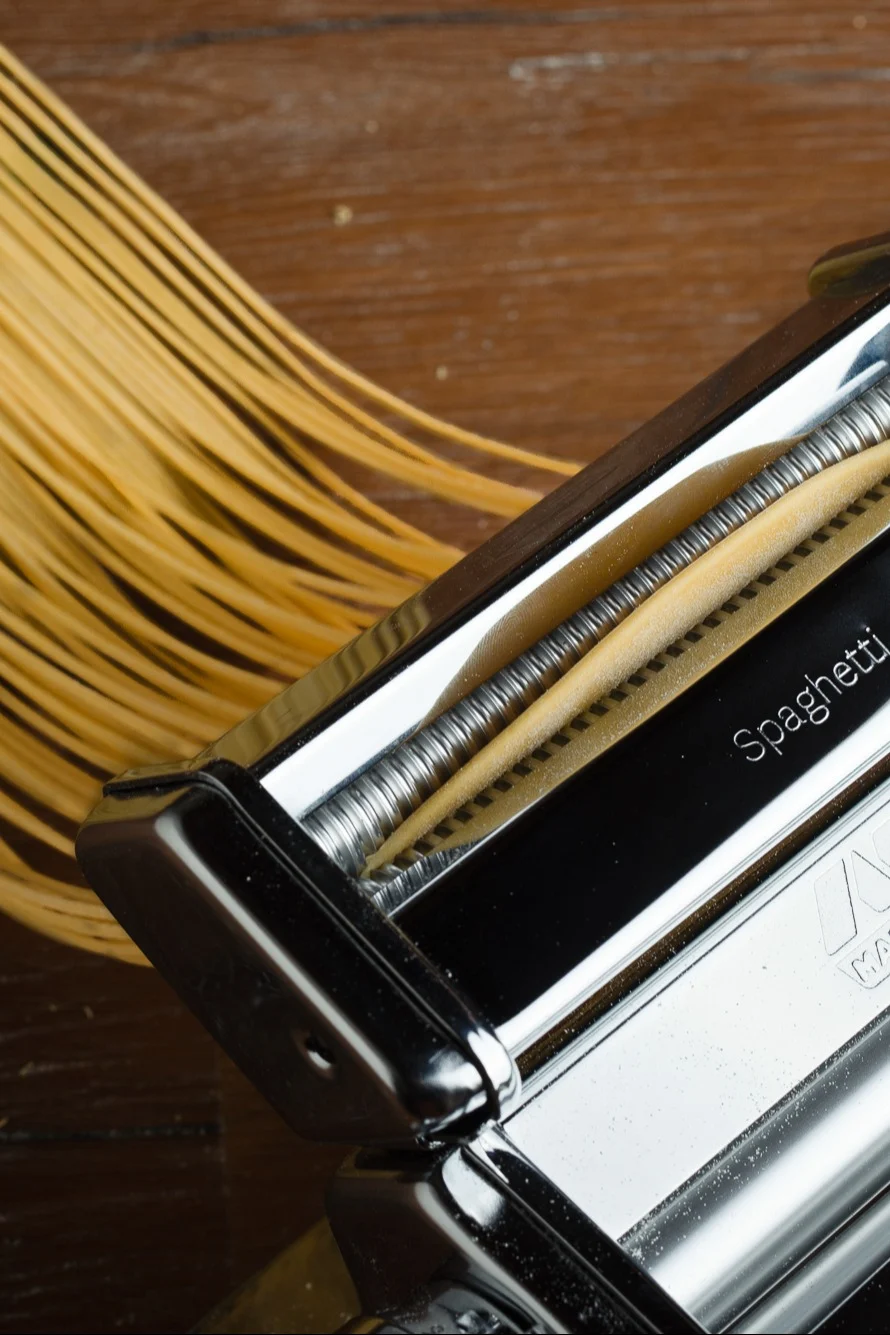 Nudelmaschine, die frische Spaghettinudeln auf eine Holzoberfläche extrudiert.