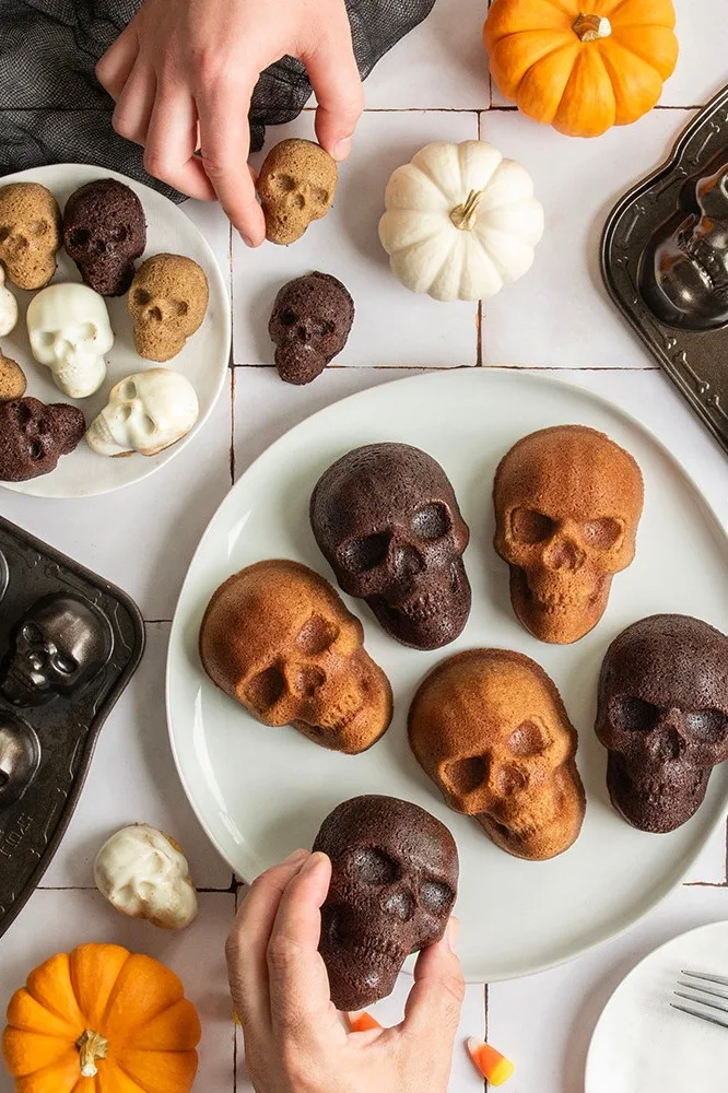 Hände arrangieren verschiedene Halloween-Totenkopfkuchen in Schoko, Vanille und Gewürzgeschmack.