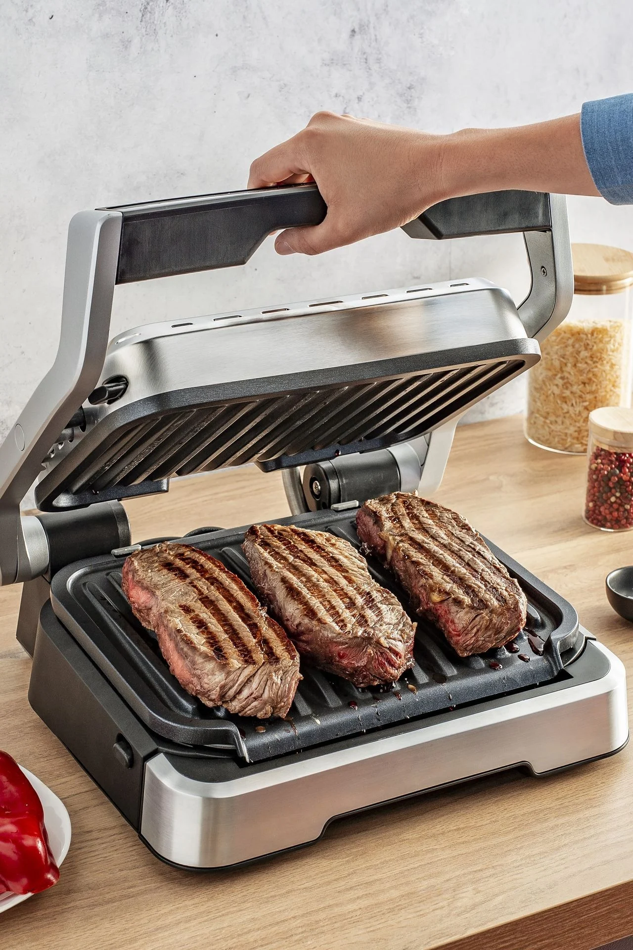 Der Optigrill von OBH Nordica steht auf einer Küchenanrichte, darauf liegen 3 Steaks.