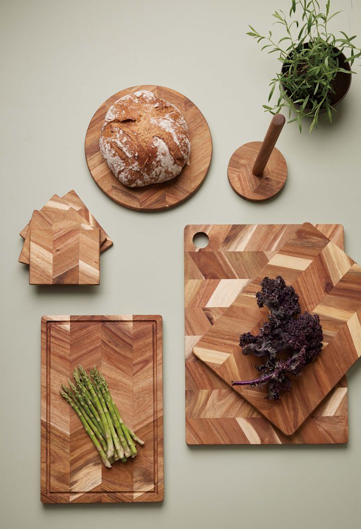 Verschiedene Größen und Formen von hölzernen Schneidebrettern mit Fischgrätenmuster von Aida, mit Brot, Frühlingszwiebeln und Kohl darauf.