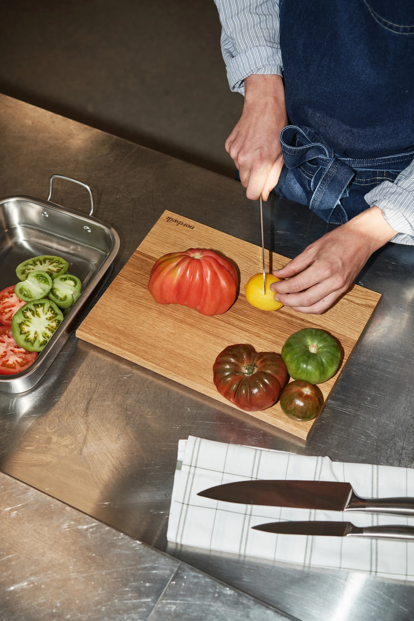 Das Messerset von Nordwik enthält alle wesentlichen Messer, die Sie zum Kochen benötigen. Hier sehen Sie eine Person in der Küche dabei, wie sie Tomaten mit einem Messer schneidet.