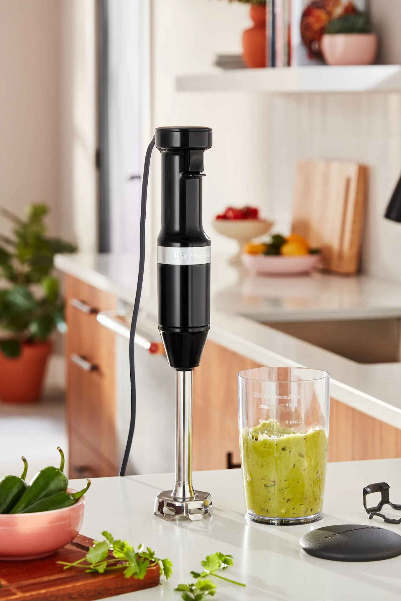 Der Stabmixer von KitchenAid steht auf einer Küchenanrichte, daneben ein Smoothie.